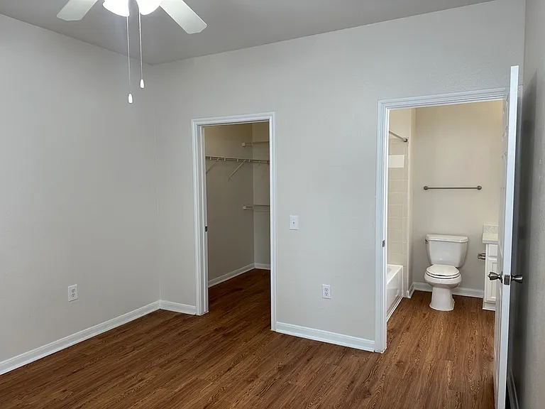 Inviting room featuring elegant wood-style flooring, a ceiling fan, spacious walk-in closet, and convenient en-suite bathroom. Inviting room featuring elegant wood-style flooring, a ceiling fan, spacious walk-in closet, and convenient en-suite bathroom.