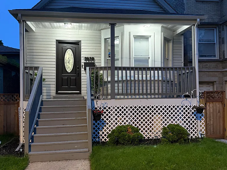 Inviting covered front porch with railings, steps, and a small landscaped yard leading to the main entry.