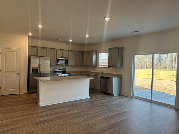 Brand new modern kitchen featuring stainless steel appliances, granite countertops, and a spacious center island. Open-concept layout with LVP flooring and sliding door access to the backyard.