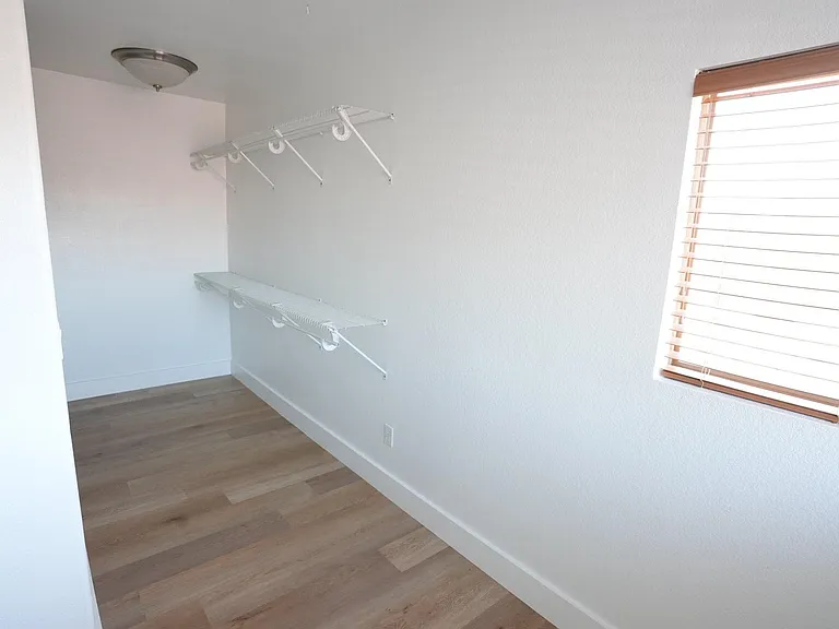Walk-in closet with dual wire shelving, durable flooring, and a window with blinds for convenient, organized storage.