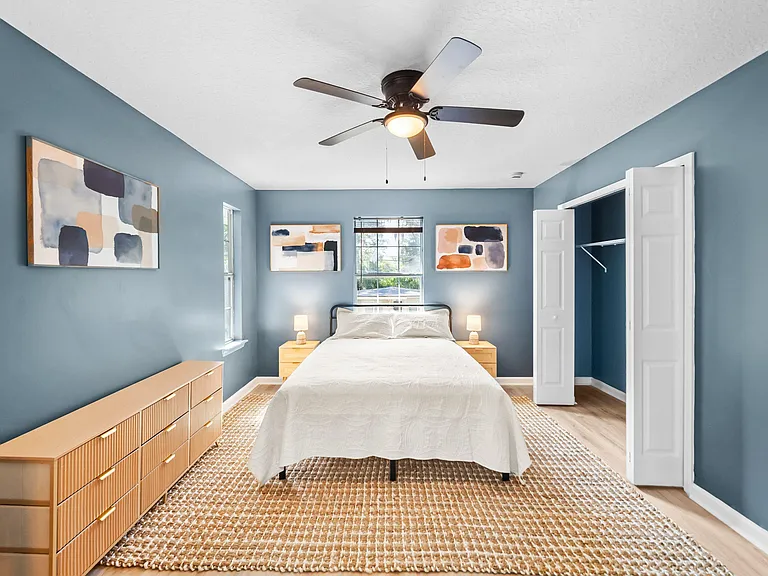 Furnished bedroom with ceiling fan, large window, and a spacious closet; includes dresser and bedside tables.