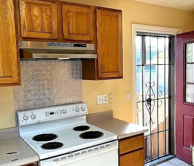 Functional kitchen with ample wood cabinetry, generous counter space, and a range hood, plus exterior door access.