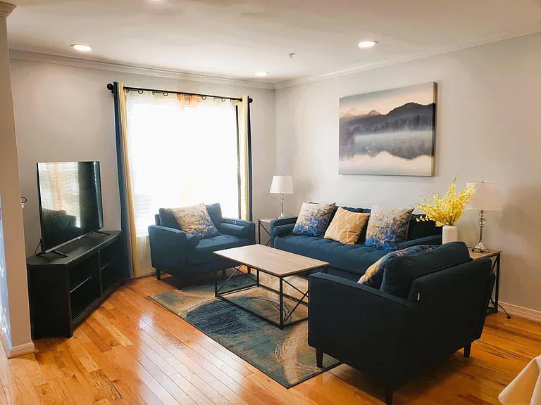 Well-appointed living room with a full seating set, coffee table, and TV area, plus a large window and hardwood floors.