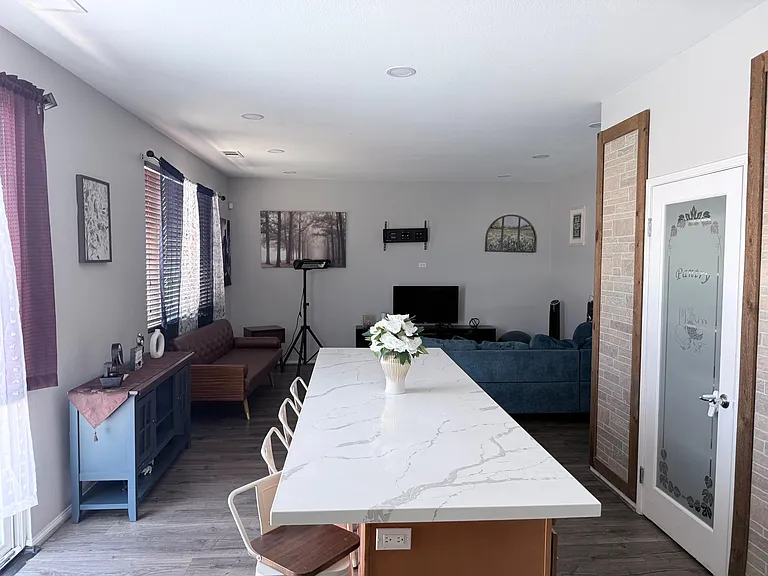 Open-concept dining and lounge area with a long island-style table, comfortable seating, and window blinds for natural light.