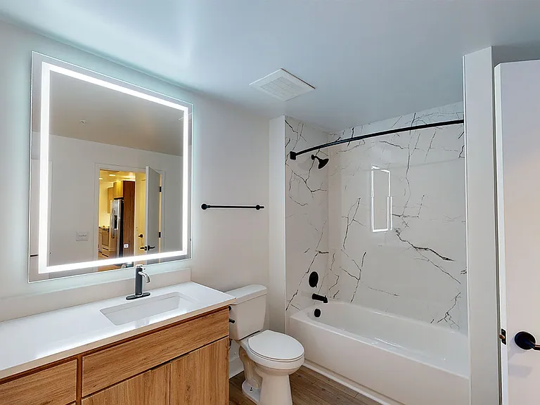 Apartment bathroom with wood-style flooring and LED vanity mirror.