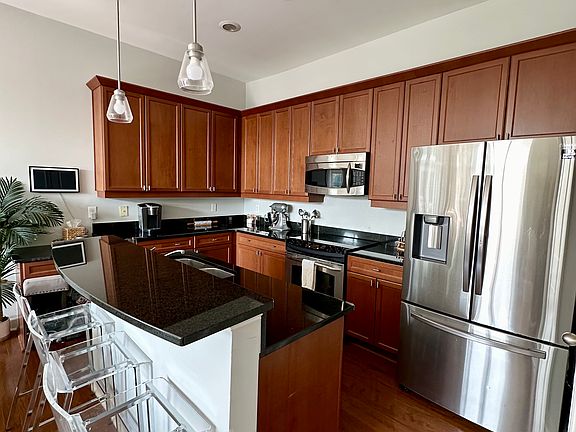 This kitchen features dark wooden cabinets that provide ample storage space, paired with sleek black granite countertops. The space is illuminated by two pendant lights hanging over the island, complemented by recessed lighting in the ceiling.