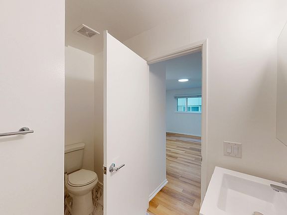 Bathroom with sink, toilet, and open door leading to a wood-floored room