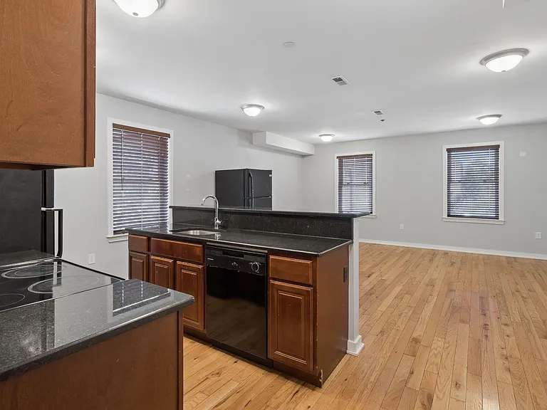 Open kitchen with breakfast bar, granite-style counters, black appliances, and hardwood floors flowing into the main living a