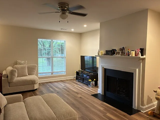 Spacious living area with ceiling fan, gas fireplace logs, recessed lighting.