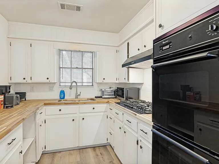 U-shaped kitchen with abundant white cabinetry, butcher-block counters, gas cooktop, wall oven, and a window over the sink.