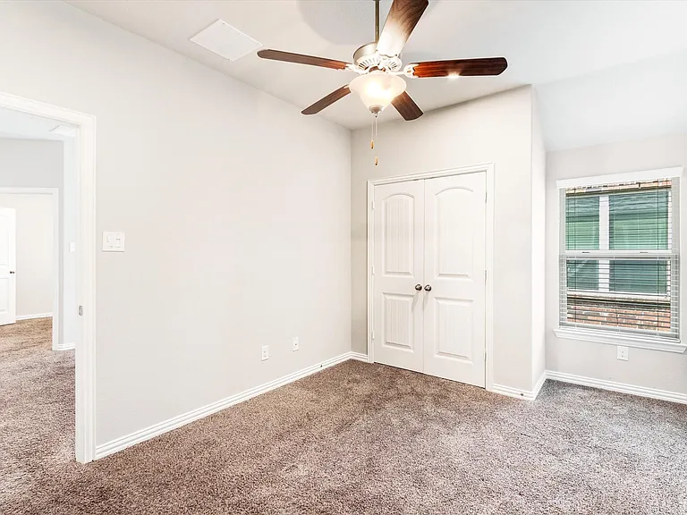 Carpeted room featuring a ceiling fan with integrated lighting, a window with blinds, and white bi-fold closet doors