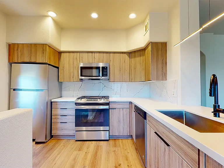 Apartment kitchen with stainless steel appliances, quartz countertops and wood-style flooring.