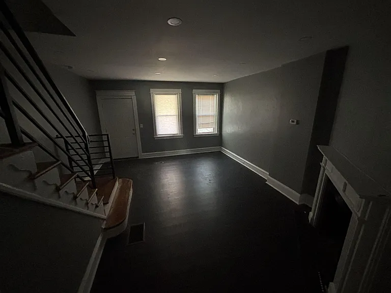 Open living area with dark flooring, recessed lighting, and two windows near the entry, plus staircase access.