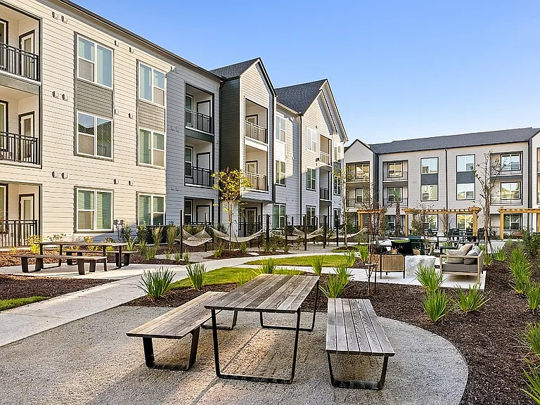Apartment outdoor amenity space with picnic tables, hammocks, soft seating, and beautifully landscaped gathering areas.