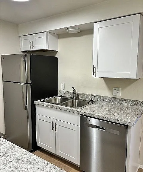 Modern kitchen with elegant granite countertops, sleek stainless steel fridge, and dishwasher for a stylish living experience.