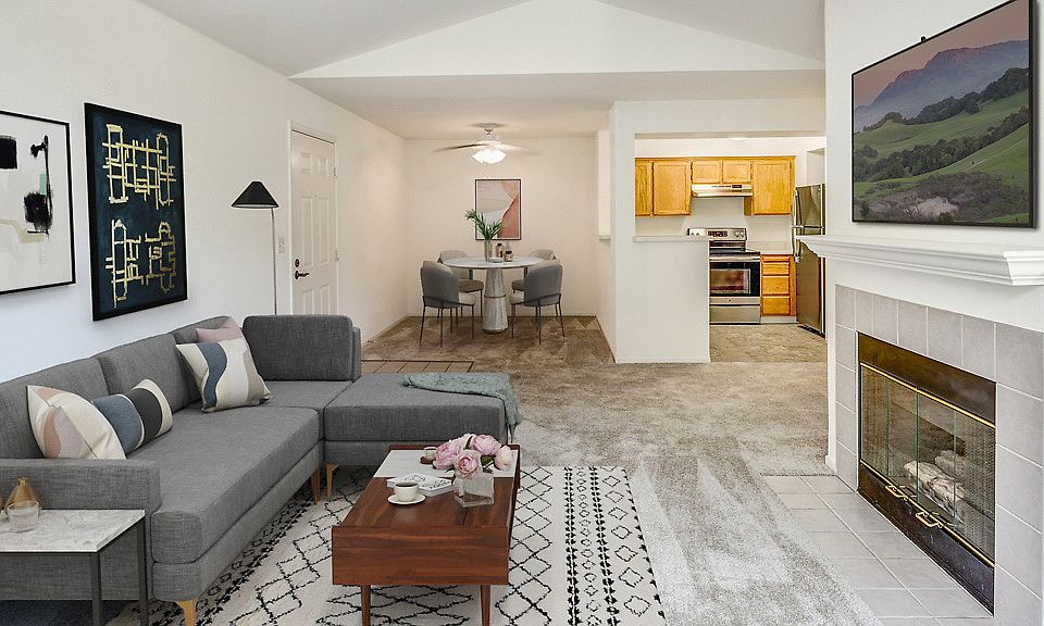 Staged living room and dining area with carpet and fireplace. Kitchen with stainless steel appliances.