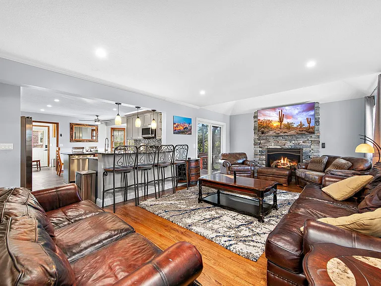 Open-concept living area with leather seating, stone fireplace, and breakfast bar connecting to the kitchen and dining space.