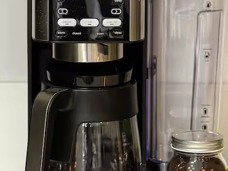 Countertop includes a spice rack, coffee and tea station, Ninja coffee maker and blender, with white stone benchtops and light timber flooring creating a fresh, welcoming feel.