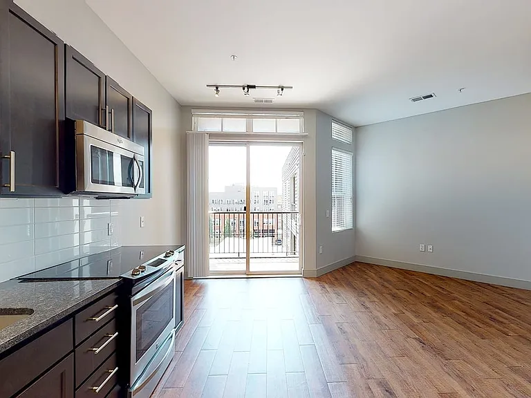 Apartment kitchen with stainless steel appliances, dining and living room with wood-style flooring and balcony or patio.