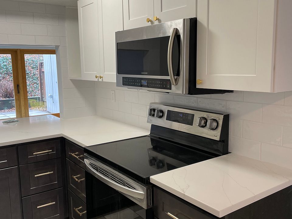 White and gray new kitchen cabinetry, quartz counter tops, full size microwave oven and smooth top stove.