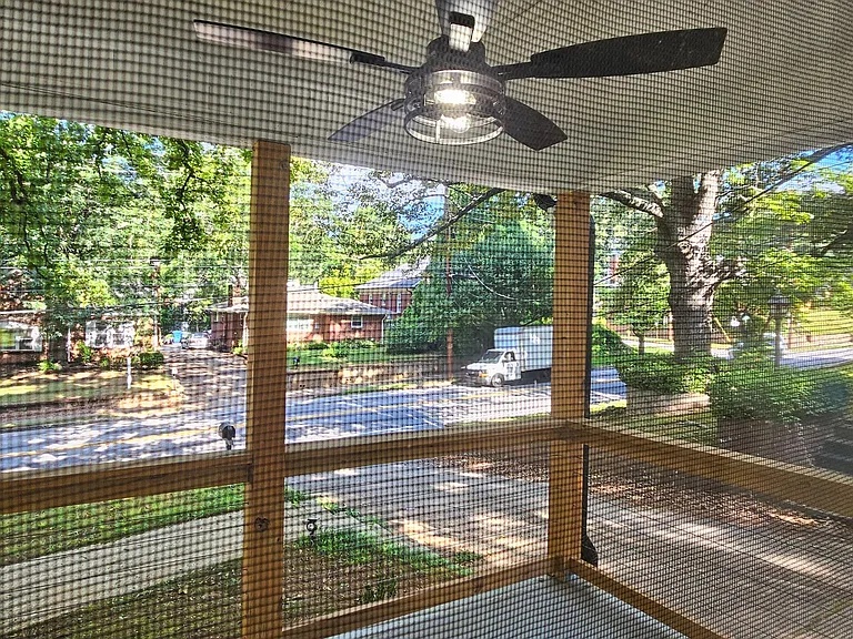 Screened-in porch with ceiling fan and elevated street views, offering an easy spot for outdoor lounging and fresh air.