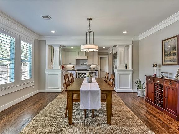 Dining room with rich crown molding is illuminated with natural light from windows overlooking the green space.
