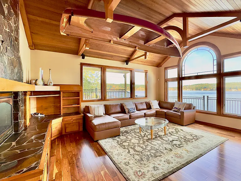 An artisan "Wineglass Wherry" floats above the living space, suspended from custom curved beams with expansive water views beyond.