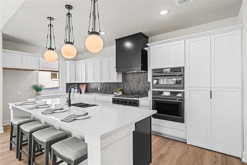 Modern kitchen with white cabinets, a large island with four cushioned stools, black appliances, and