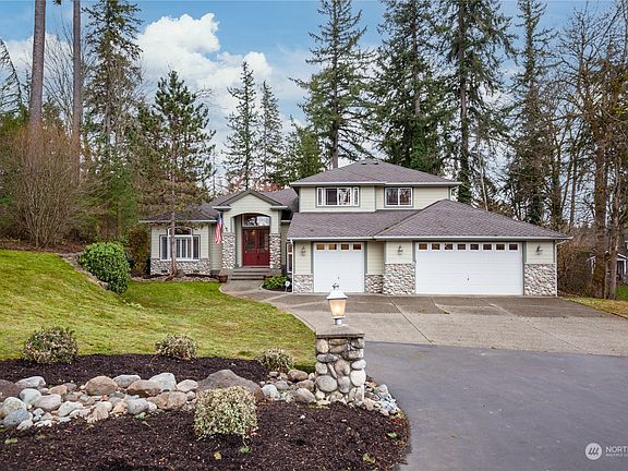 A street view of the home, with mature trees in the background.  The grounds have been professionally landscaped.>