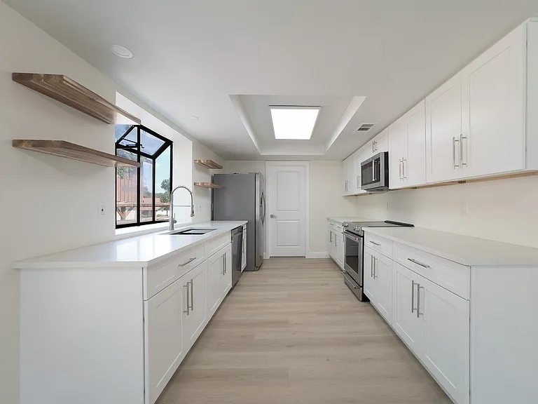 Kitchen with beautiful casement window over sink, electric stove, microwave, and fridge. Pantry door shown at end of kitchen.