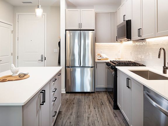 Modern with grey cabinetry, white quartz countertops, white tile backsplash, and stainless-steel appliances