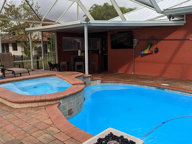 Propane powered fire feature doubles as a fountain/water feature. Note a flat screen TV and soundbar in the background for added outdoor entertainment and an outdoor shower for rinsing off before/after pool use.