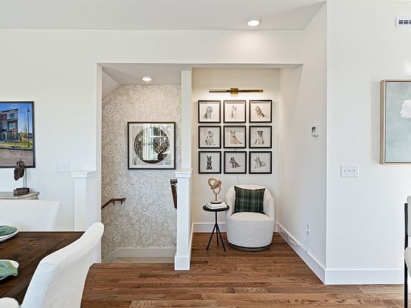Modern living space with wood floors, art on the walls, a round chair, and a decorated staircase noo