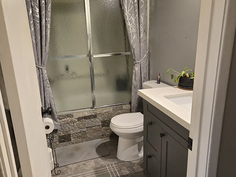 Bathroom, shower/tub with rainfall showerhead. Vanity has a granite countertop. The tub has fake stucco brick for detail. Curtains can stay.