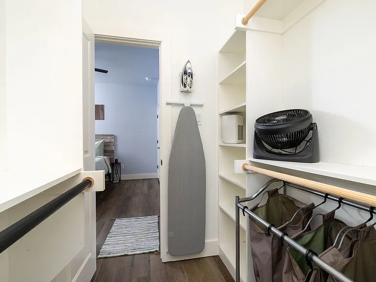 Primary bedroom walk-in closet featuring iron, ironing board and portable fan.