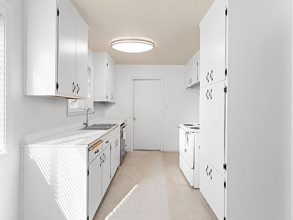 Freshly painted kitchen featuring rejuvenated cabinetry, two large windows with new blinds, ample counter and storage space, and a convenient double sink.