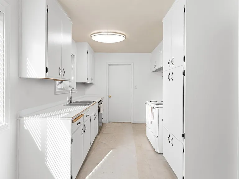 Freshly painted kitchen featuring rejuvenated cabinetry, two large windows with new blinds, ample counter and storage space, and a convenient double sink.