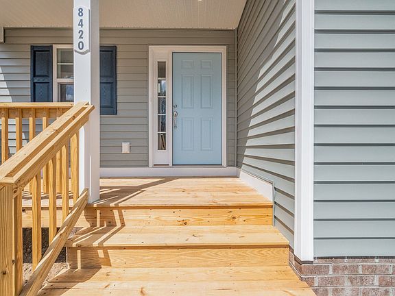 A light blue front door of a house with gray siding, wooden porch, and number 8420 visible next to t