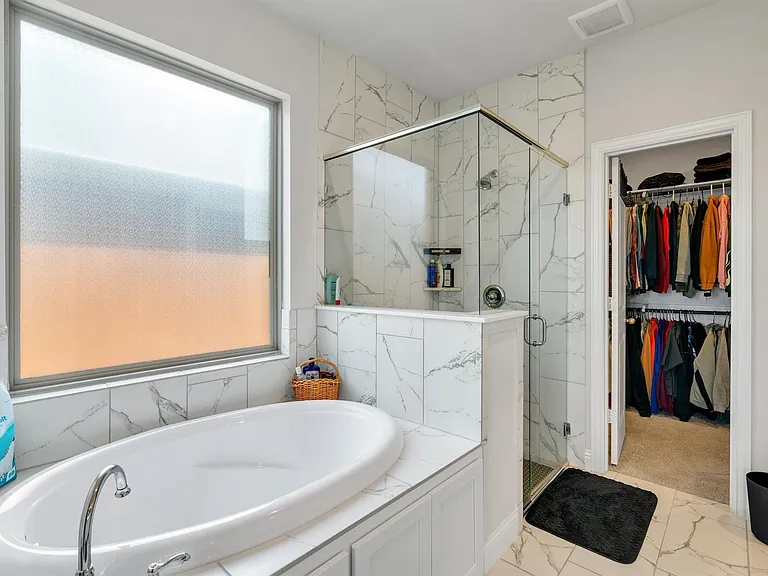 Freestanding oval soaking tub with chrome fixtures, surrounded by large format marble-look tile