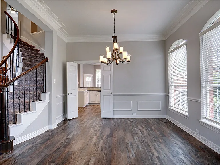Elegant interior featuring wood-finish flooring, a contemporary chandelier, and a curved staircase with wrought iron balusters