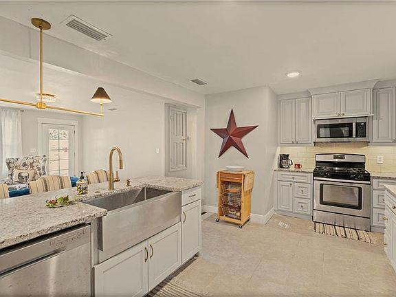 Kitchen featuring stainless steel appliances, light stone countertops, decorative light fixtures, and white cabinets