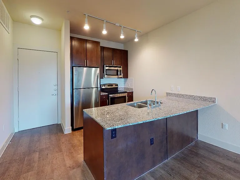 Apartment kitchen with stainless steel appliances in select homes, granite countertops and wood-style flooring.