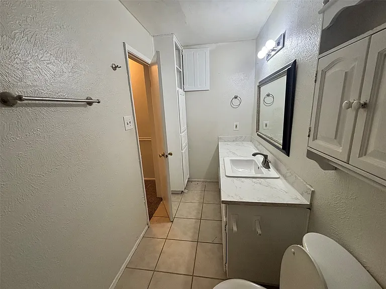 Bathroom featuring a single vanity with a white countertop and integrated sink, a framed mirror, and overhead lighting