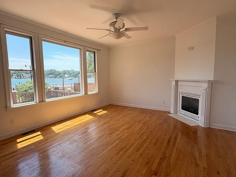 Open-concept sitting room off the kitchen with wall of lake-view windows, hardwood floors and a cozy fireplace_ideal for morning coffee, casual chats or unwinding with water views.