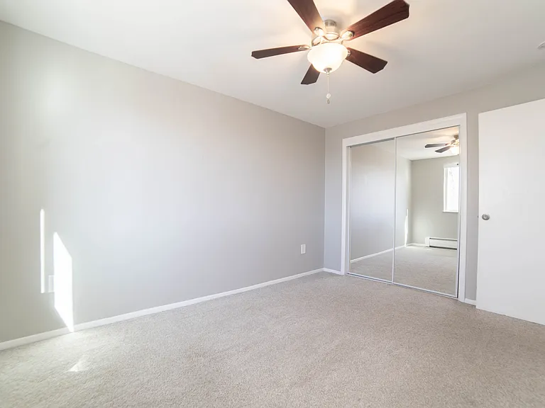 Bright and airy bedroom with plush carpeting, mirrored closet doors, and a modern ceiling fan.