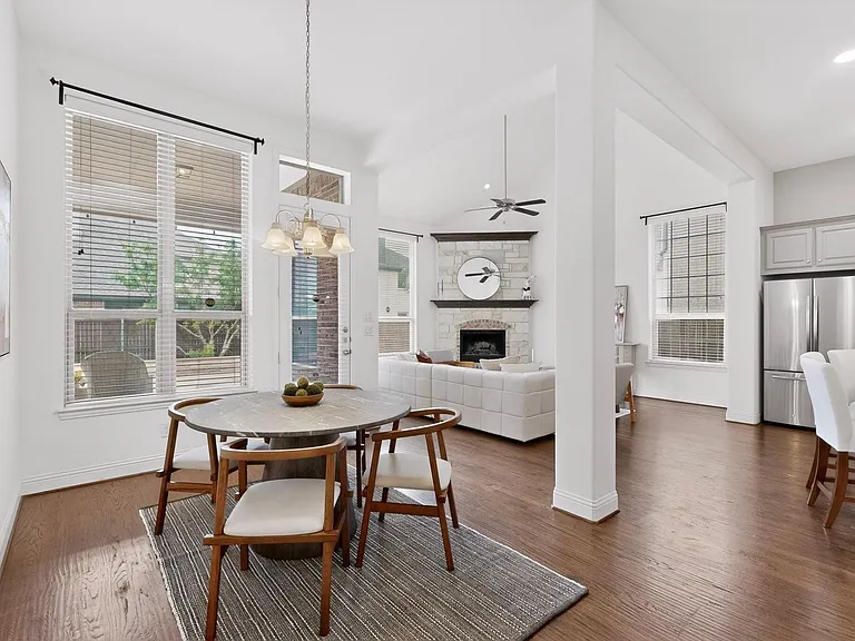 Spacious dining area showcasing elegant hardwood floors, tall windows and a chandelier, blending style and comfort for everyday living.