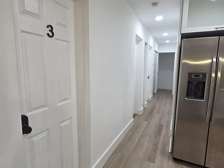 Clean hallway with durable flooring and recessed lighting, connecting multiple rooms and the nearby kitchen.