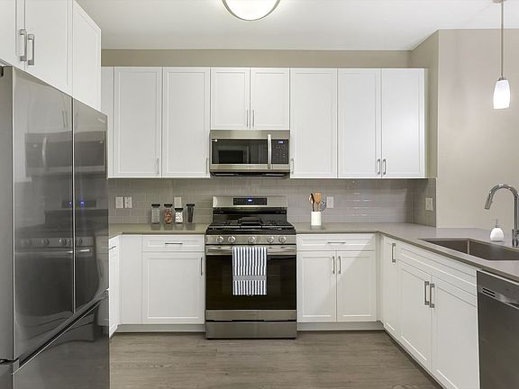 Renovated Package II kitchen with grey quartz countertops, white cabinetry, grey tile backsplash, stainless steel appliances, and hard surface flooring