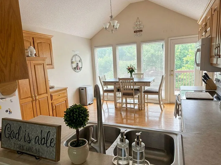 Eat-in kitchen with ample wood cabinetry, full appliance setup, and a dining nook by large windows with deck access.