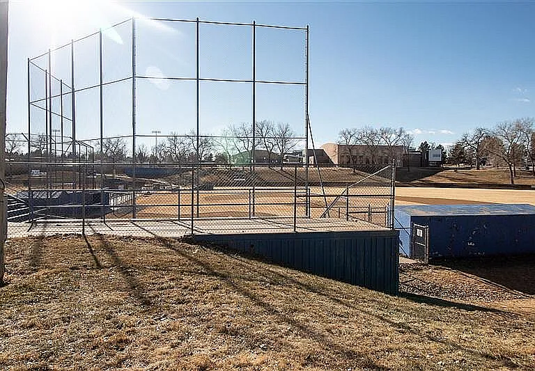Charming baseball field under clear blue sky, featuring well-maintained diamond and backstop, surrounded by lush greenery and trees.